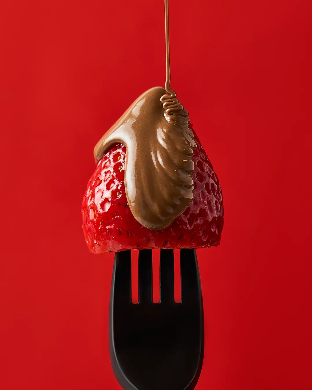 Fresa bañada en chocolate sobre tenedor, fotografía publicitaria de alimentos